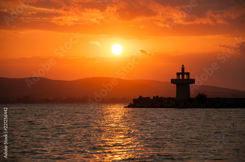 Lighthouse against a beautiful evening sunset on the sea. Amazing sunset on black sea and beautiful cloudscape.