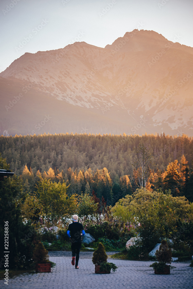 Obraz premium Silhouette of athlete in nature. Man watching sunset in mountains by beautiful lake. Sport photo, edit space. High Tatras Slovakia. Morning warm up concept photo