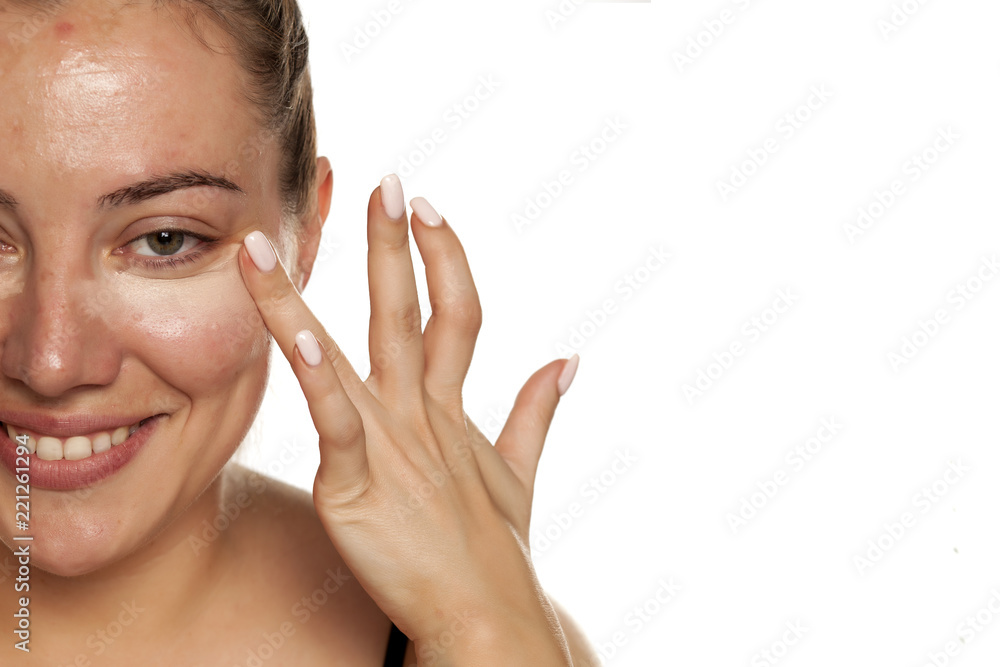 Young woman applying concealer under her eyes with brush on white background Young woman applying concealer under her eyes with brush on white background