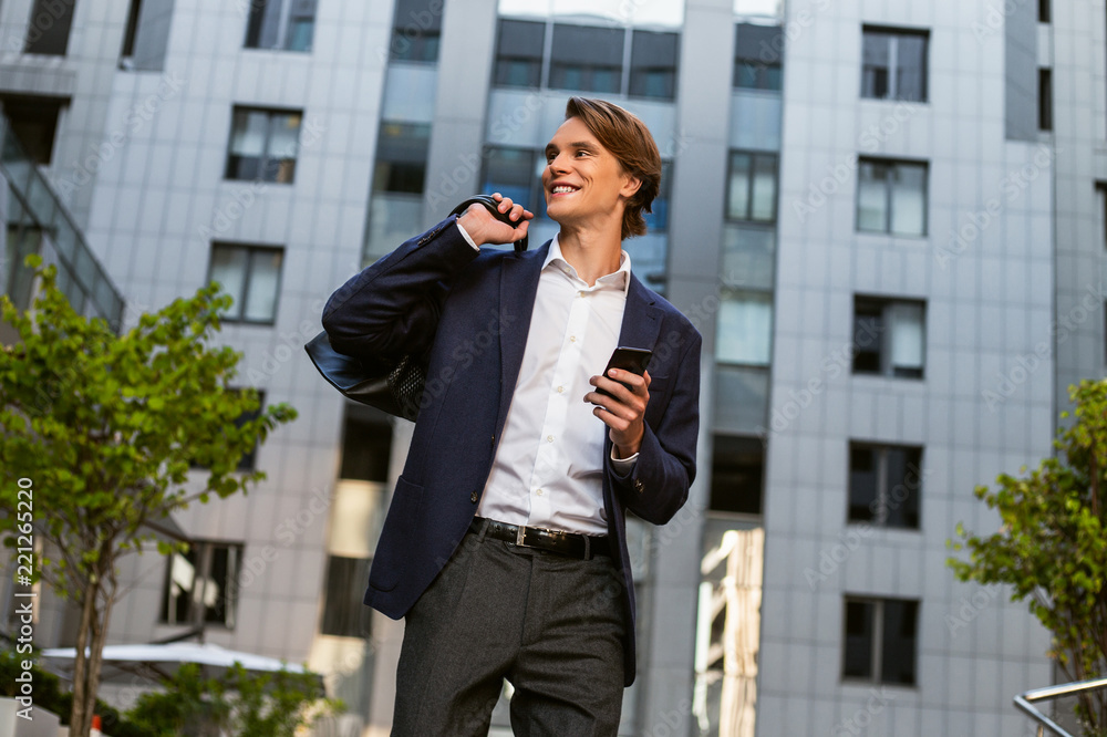 You have one unread message. Handsome young man carrying his bag and using his smartphone with smile while standing outdoors You have one unread message. Handsome young man carrying his bag and using his smartphone with smile while standing outdoors