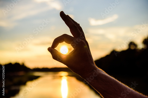 Silhouette ok hand gesture in front of sunset above river water surface. Sunset sunlight romantic atmosphere. Top places to visit in evening. Ok gesture sign of best choice approve and confirm