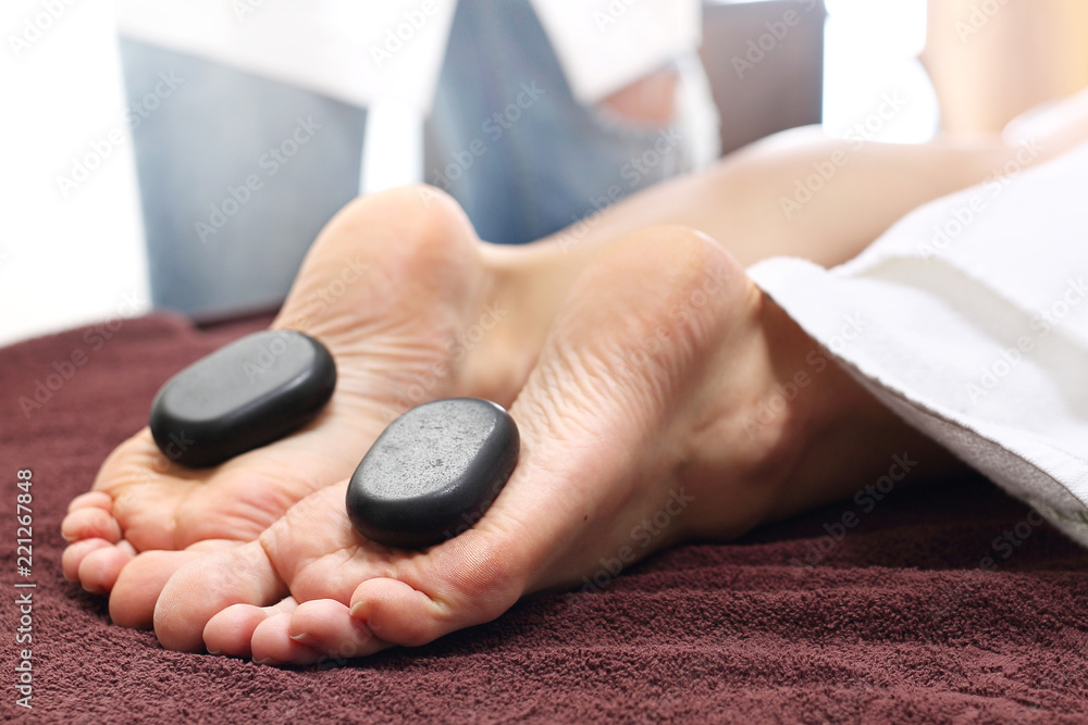 Relaksacyjny masaż kamieniami. Kobiece stopy z kamieniami bazaltowymi, relaks w salonie spa. - obrazy, fototapety, plakaty 