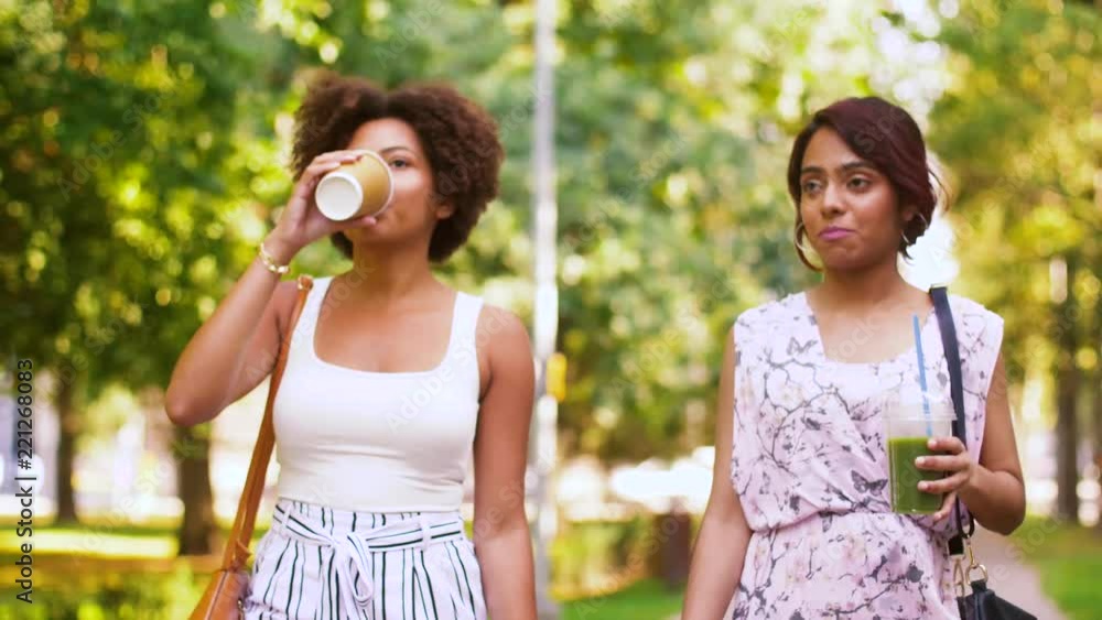 leisure and friendship concept - happy women or friends with drinks walking along summer park leisure and friendship concept - happy women or friends with drinks walking along summer park