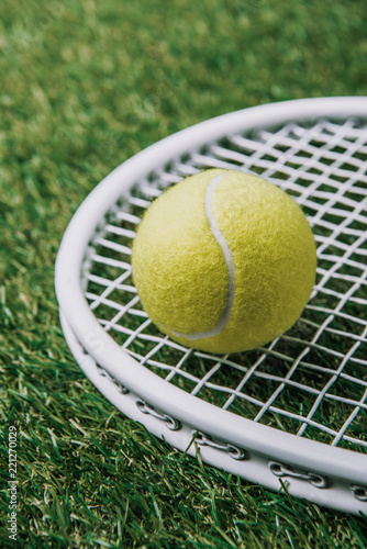 close up view of tennis ball on racket lying on green lawn