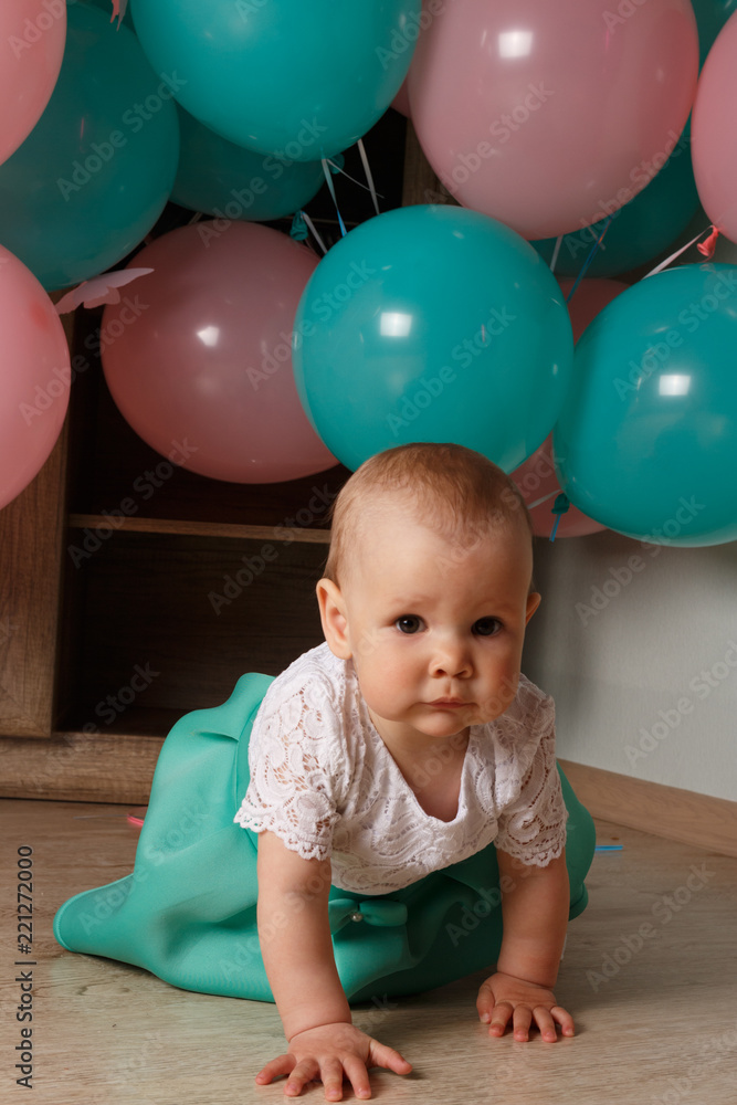 A small, charming child, a girl, celebrates her first birthday, sitting next to her with balloons. Children's Party Organization.