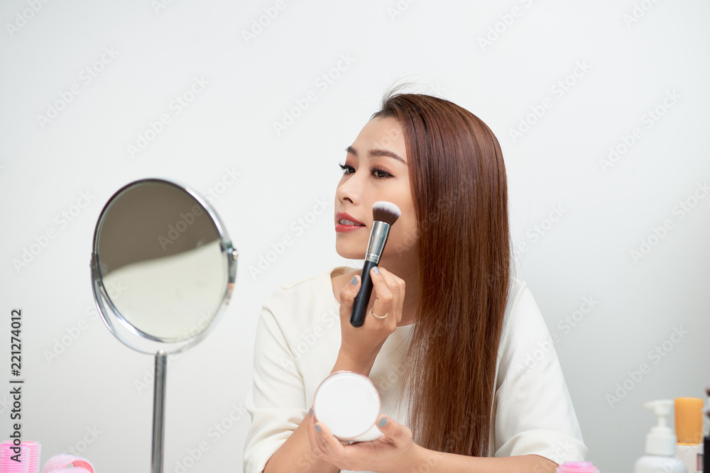 young beautiful woman applying her make-up with a big brush , looking in a mirror young beautiful woman applying her make-up with a big brush , looking in a mirror