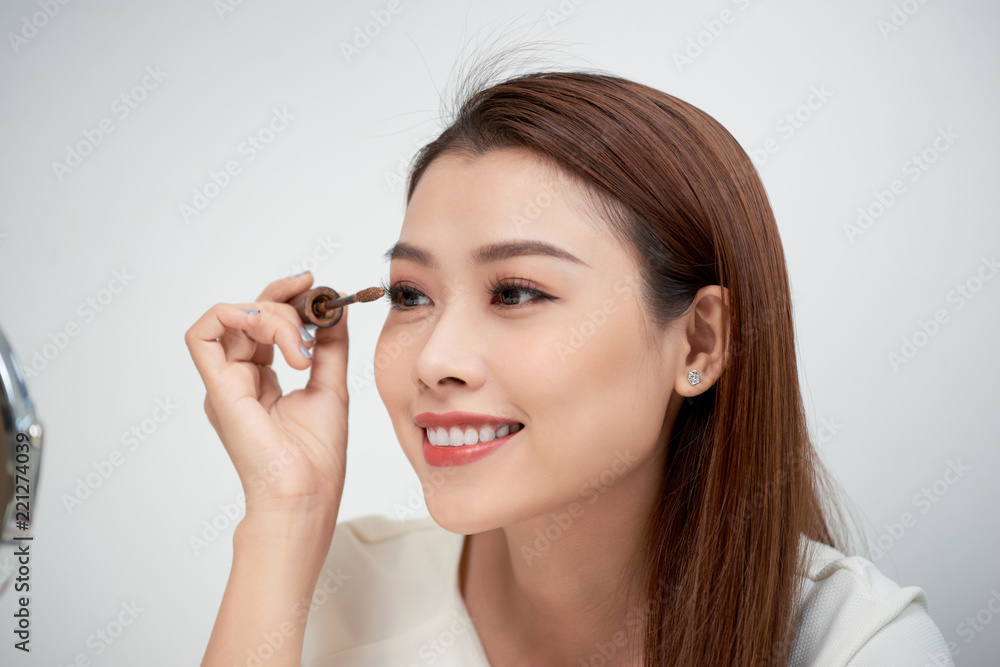 Beauty model teenage girl looking in the mirror and applying mascara make up. Beautiful young woman apply makeup Beauty model teenage girl looking in the mirror and applying mascara make up. Beautiful young woman apply makeup