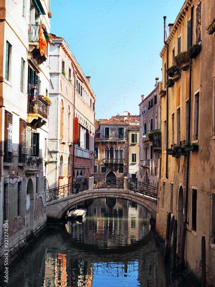 The canal is surrounded with the bridge by ancient buildings, gondolas and boats in Venice
