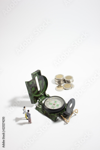 Miniature businessman with compass and coins verticle.