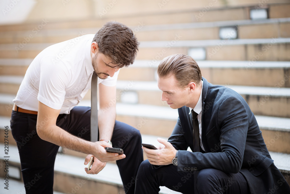 Business partners talking about new project in the city on break. They are use smartphone discussing at stairway. Business partners talking about new project in the city on break. They are use smartphone discussing at stairway.