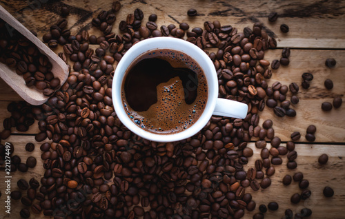 Black coffee in white cup, with coffee beans on wooden background, top view