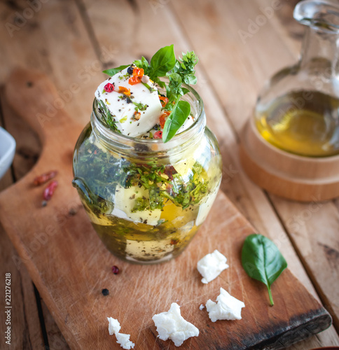 Close-up of marinated feta cheese in olive oil, herbs and red pepper flakes on wooden background 