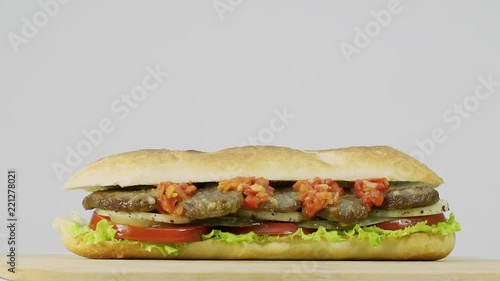 Turkish fast food meatball sandwich with cheese, red sauce with vegetables. Rotating shot.