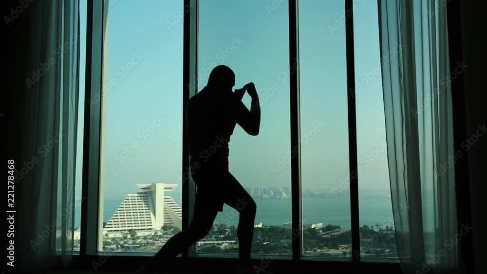 Man trains near big window in hotel room, shadow boxing. View of coast of the Persian Gulf in Doha - capital and most populous city in Qatar, Arabian Peninsula, Middle East Man trains near big window in hotel room, shadow boxing. View of coast of the Persian Gulf in Doha - capital and most populous city in Qatar, Arabian Peninsula, Middle East