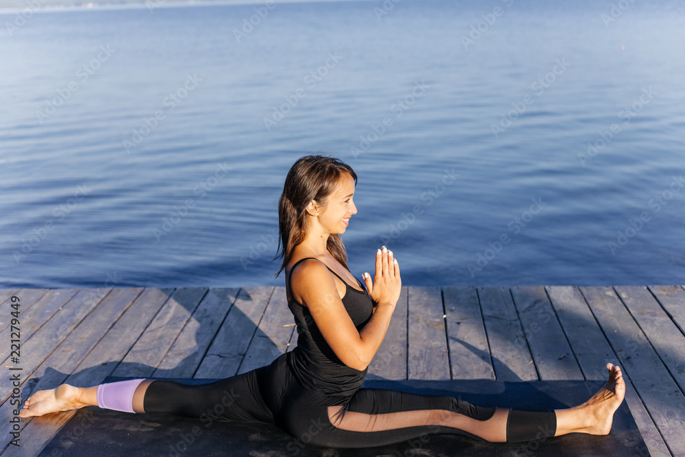 Young attractive smiling woman practicing yoga on a lake