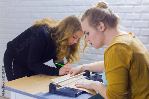 Two professional women decorators, designers working with kraft paper and using paper cutter, guillotine at workshop, studio. Crafting work, decoration and art concept