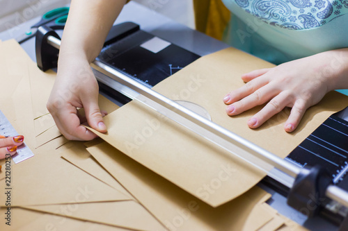 Close up shot - professional woman decorator, designer working with kraft paper and using paper cutter, guillotine at workshop, studio. Crafting work, decoration and art concept photo