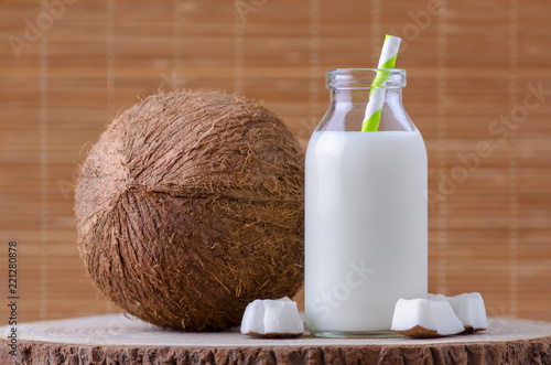 coconut milk in glass bottle with tubule on natural wooden brown background