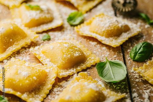 Raw ravioli with basil and flour on wooden