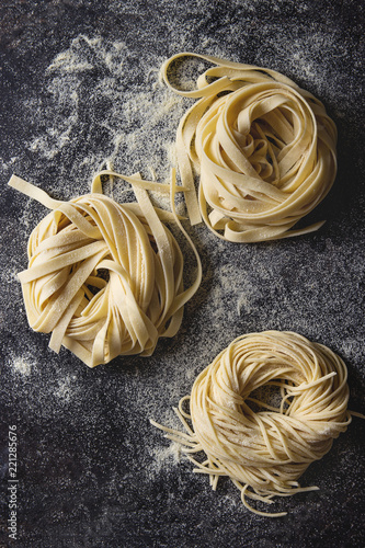 Variety of italian homemade raw uncooked pasta spaghetti and tagliatelle with semolina flour over black texture background. Flat lay, space