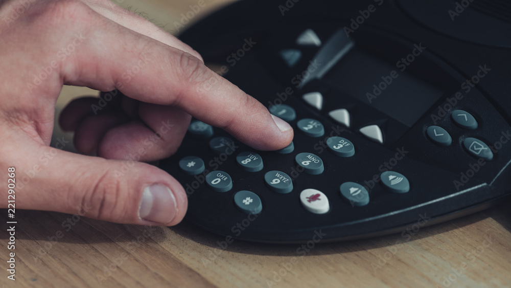 cropped shot of man pushing button of conference phone on wooden table cropped shot of man pushing button of conference phone on wooden table