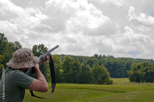A man trap shooting with a 12 gauge shotgun on a beautiful summer day with big white clouds in the sky and a forest treeline in the background in Pennsylvania, USA