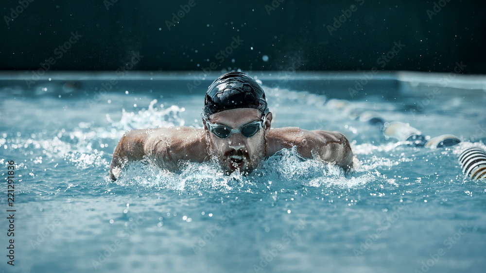 The dynamic and fit swimmer in cap breathing performing the butterfly stroke at pool. The young man. The fitsport, swimmer, pool, healthy, lifestyle, competition, training, athlete, energy concept