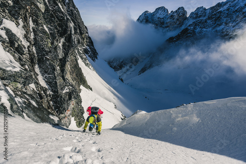 An alpinist climbing steep ice wall. A winter alpine ascent in alpine landscape. Adventure and extreme climb in snow and ice to a summit of a peak. Solo climber in winter mountains.