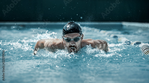 The dynamic and fit swimmer in cap breathing performing the butterfly stroke at pool. The young man. The fitsport, swimmer, pool, healthy, lifestyle, competition, training, athlete, energy concept © master1305