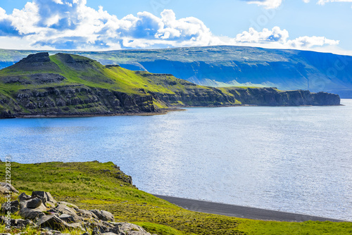 Beautiful rugged volcanic basalt rock Iceland coastline blue skies and low clouds. Green moss and grass covered hills