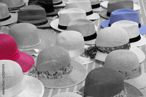 A close view of many Panama straw hats on a cotton sheet on sale on a street by a peddler. All black and white except one red hat and one blue hat