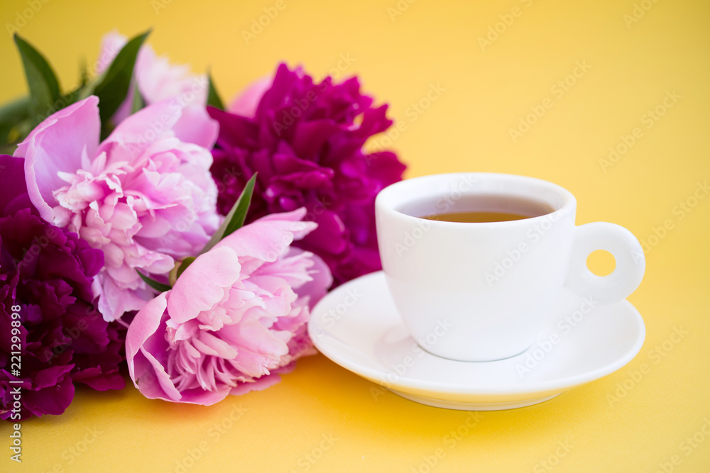 Cup of tea on a saucer and bouquet of pink peonies on a yellow background
Cup of tea on a saucer and bouquet of pink peonies on a yellow background
