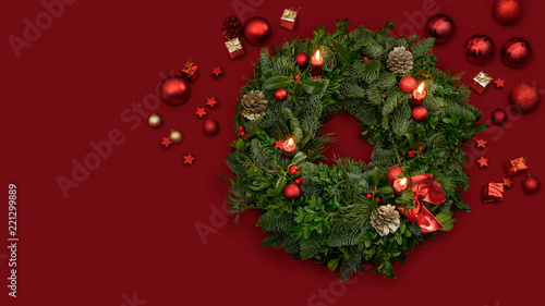 Traditional advent wreath of green fir twigs and mistletoes with red candlelight and shiny baubles gifts and stars on a red surface, studio shot with copy space, no people