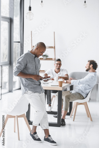 african american man using tablet while colleagues discussing strategy at workplace in office