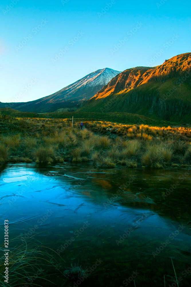Wild freezing nature scenery in the cold morning, sun is rising and covering huge mountains, volcano and alpine valley, frozen deep lake in the front, New Zealand Tongariro National park