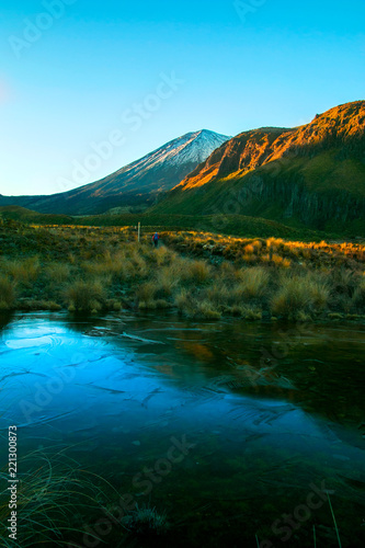 Wild freezing nature scenery in the cold morning, sun is rising and covering huge mountains, volcano and alpine valley, frozen deep lake in the front, New Zealand Tongariro National park