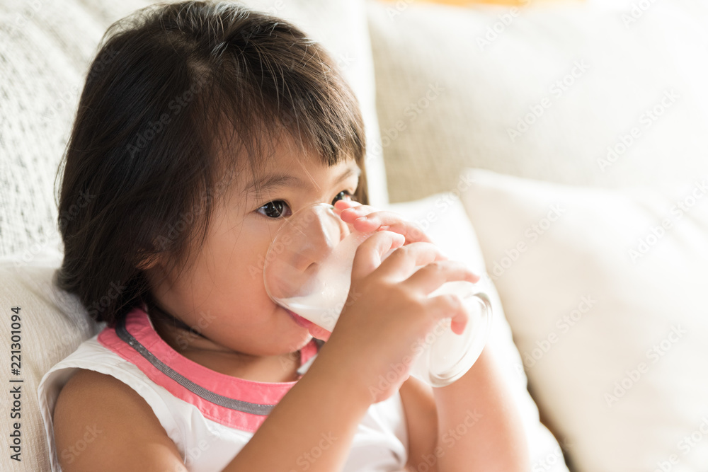 Happy little asian girl hand holding drinking milk glass, sitting on sofa at home. Medicine and health care concept. Happy little asian girl hand holding drinking milk glass, sitting on sofa at home. Medicine and health care concept.