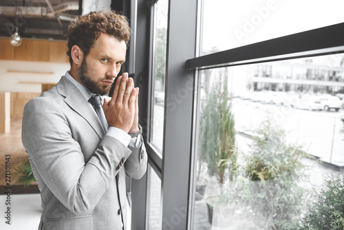 portrait of caucasian businessman standing at window in office and praying