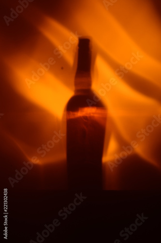 Background. The shadow of the bottle of vine and the reflection of fire on the wall.