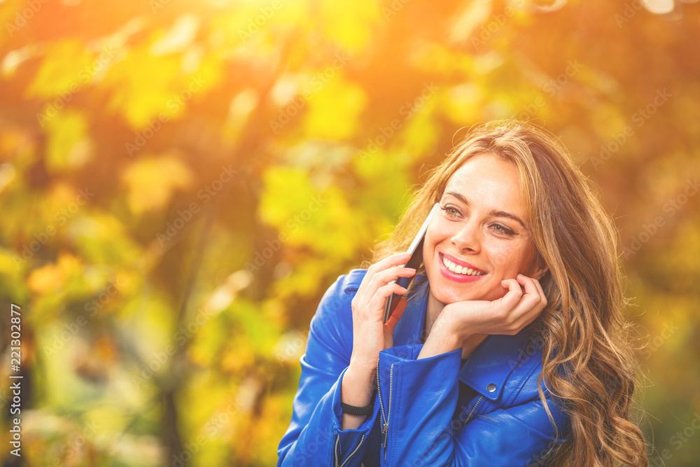 Cute young woman using smartphone in the park with autumn season colors. Cute young woman using smartphone in the park with autumn season colors.