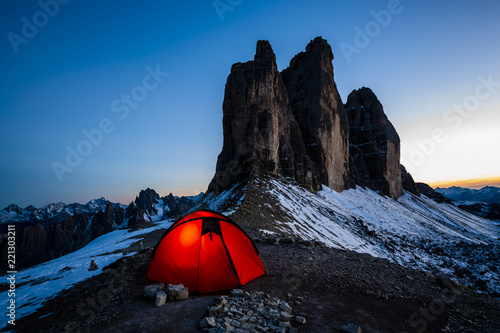 Night bivouac at Tre Cime di Lavaredo, milion star hotel under night sky, red illuminated tent on pass in Dolomites, Italy.