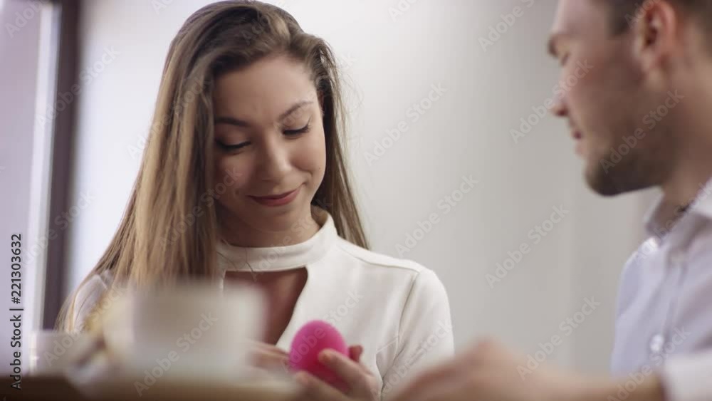 Two young people is sitting in a cafe. Man and woman are smiling and sitting in the cafe at the table during break. Couple is talking and drinking coffee. He proposes marriage Two young people is sitting in a cafe. Man and woman are smiling and sitting in the cafe at the table during break. Couple is talking and drinking coffee. He proposes marriage