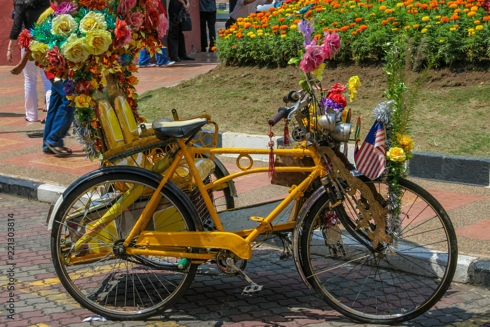 Great close-up of a yellow trishaw nicely decorated with colourful flowers, a flag and other trinkets which is a popular transportation for tourists in Malacca, Malaysia.