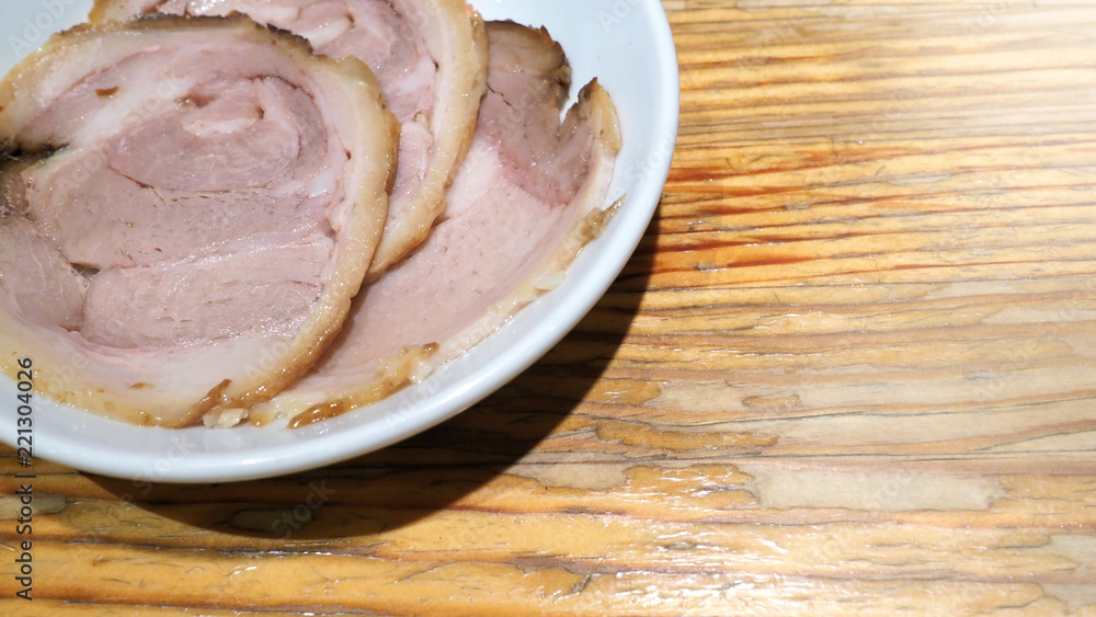 Chashu pork 3 pieces slice on the white color dish and wood table which additional menu for topping on tonkotsu ramen famous traditional food in Sapporo Hokkaido Japan. Chashu pork 3 pieces slice on the white color dish and wood table which additional menu for topping on tonkotsu ramen famous traditional food in Sapporo Hokkaido Japan.