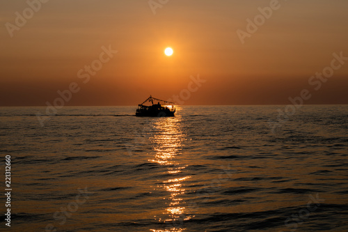 The silhouette of a ship sailing on the sea on the backdrop of the setting sun and a sun track on the water