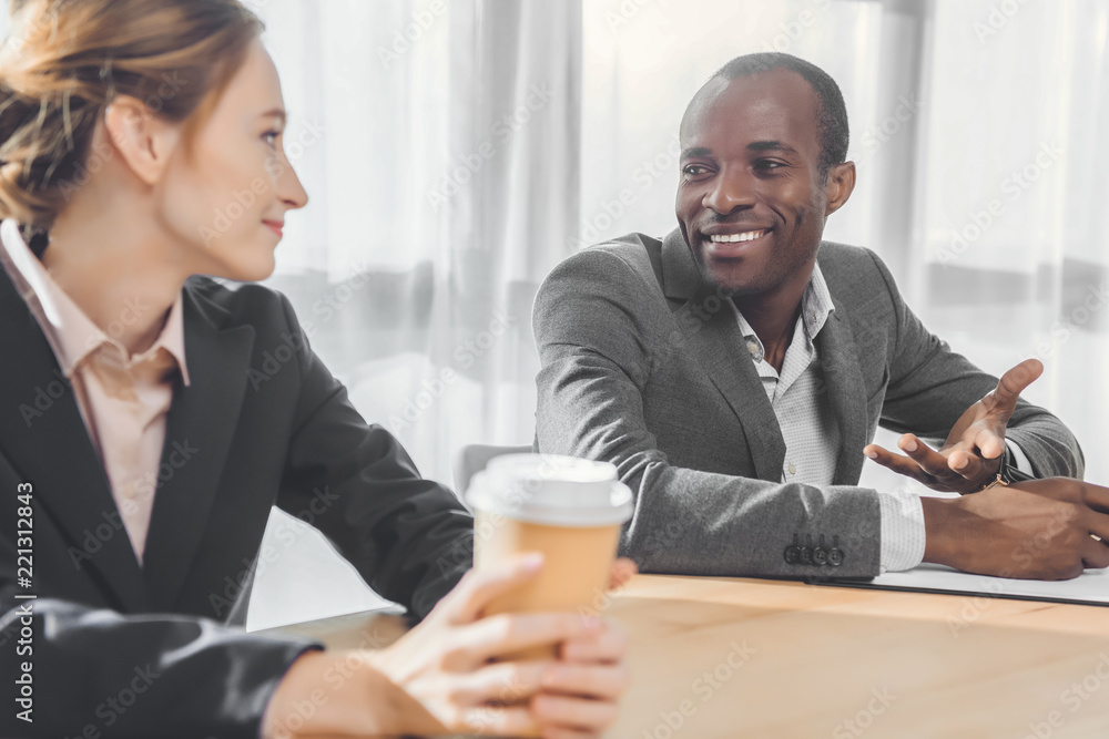 african man smiling to woman with coffe in hands at office space african man smiling to woman with coffe in hands at office space