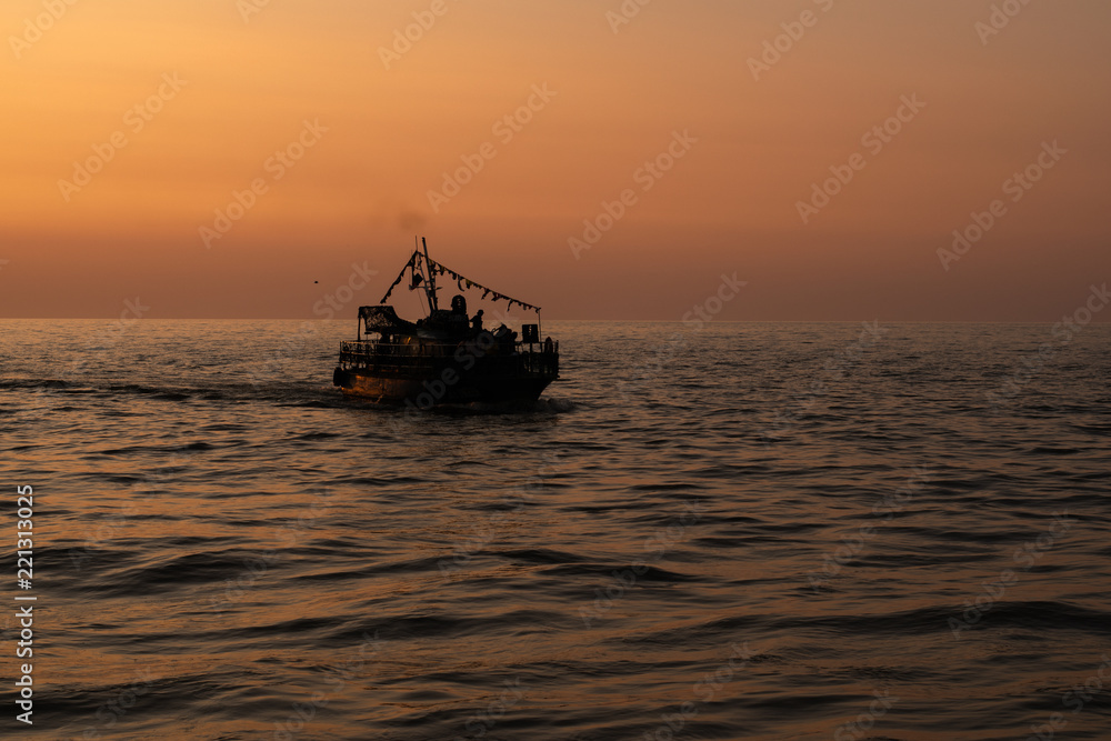 Silhouette of a ship sailing on the sea against the orange sunset sky