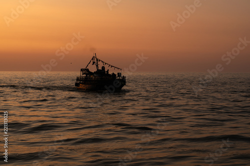 Silhouette of a ship sailing on the sea against the orange sunset sky