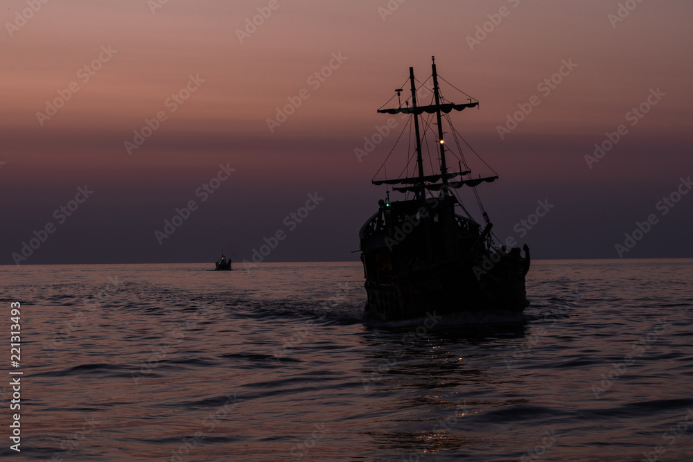 Two silhouettes of ships floating on the sea against the darkening sky
