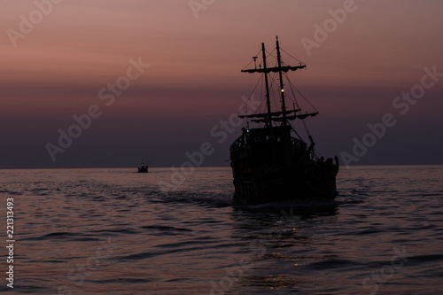 Two silhouettes of ships floating on the sea against the darkening sky